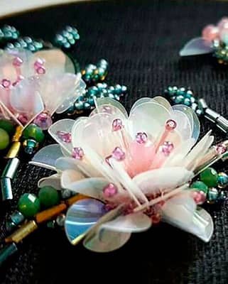Flor bordada en 3D con pétalos de lentejuela iridiscente, canutillos y perlas rosadas.
