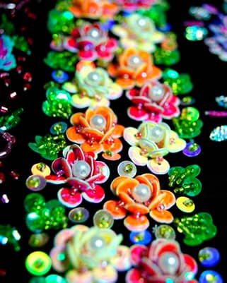 Flores bordadas con lentejuelas 3D en colores vibrantes, perlas centrales y pedrería verde.